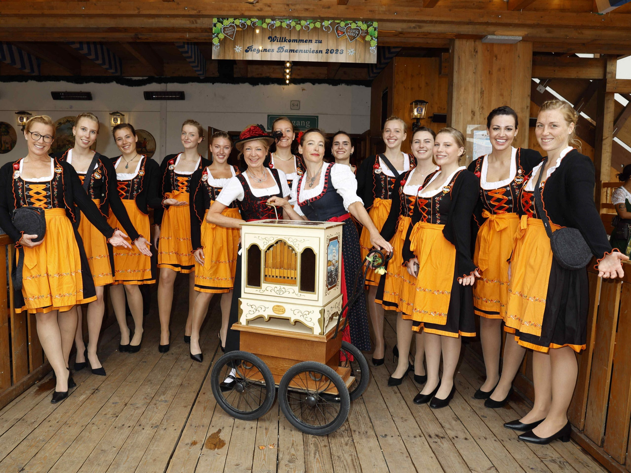 Hostessen im schwarz-weiß-orangenen Dirndl bei den SIXT Damenwiesen lächeln in die Kamera, stilvoller Promotion Einsatz von cinnamon mit eleganten Hochsteckfrisuren auf dem Oktoberfest
