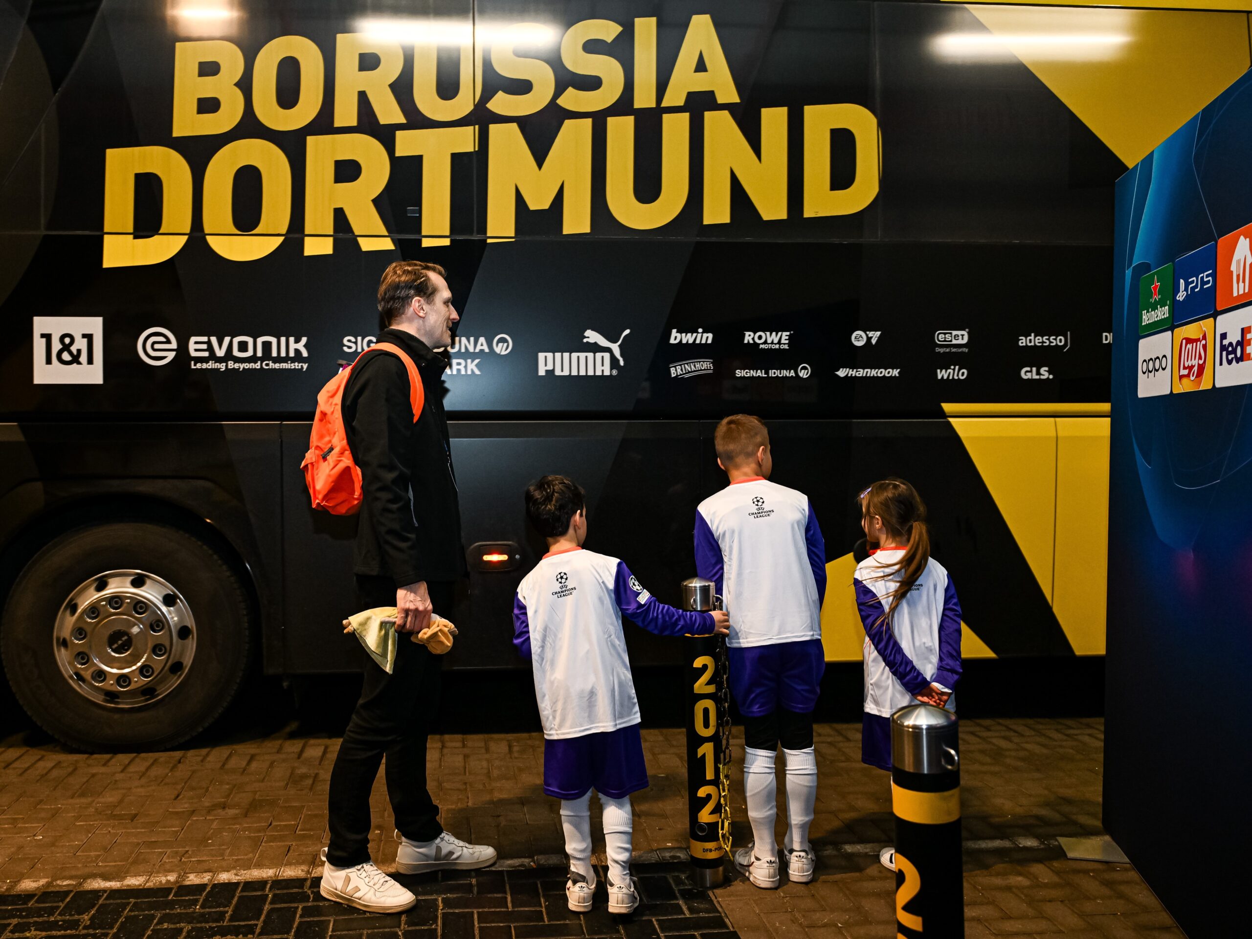 Drei Kinder im Fußball-Outfit und ein Mann in Sportkleidung stehen vor dem Borussia Dortmund Bus mit dem Rücken zur Kamera, sportliche Promotion bei Event und Fanaktion