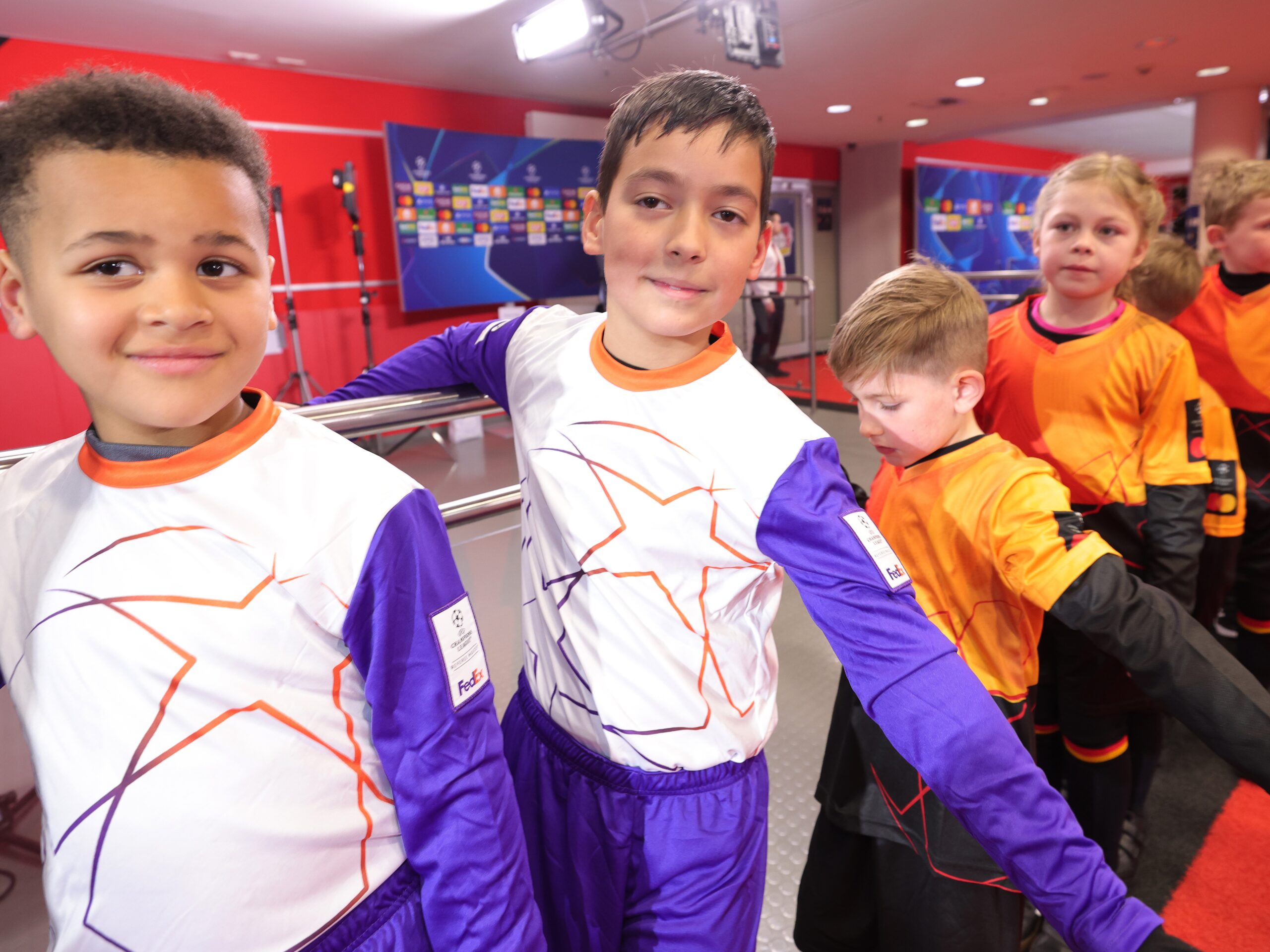 Kinder in Fußball-Outfits warten auf den Stadioneinlauf mit Fußballspielern und blicken in die Kamera, emotionale Sportevent- und Fanaktion im Stadion