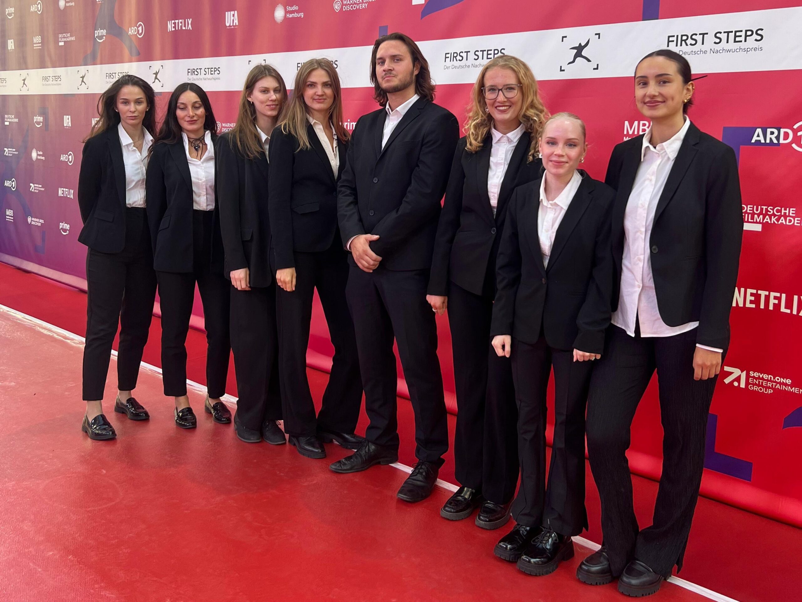 Hostessen in weißen Hemden und schwarzen Anzügen vor einer Fotowand bei einer Premiere in Berlin, eleganter Empfangsservice für Gala und Event.
