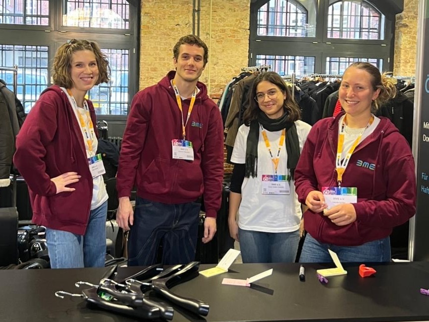 Vier Hosts und Hostessen in weinroten Hoodies und Blue Jeans arbeiten an der Garderobe in Freiburg, professioneller Empfangsservice bei Event und Veranstaltung