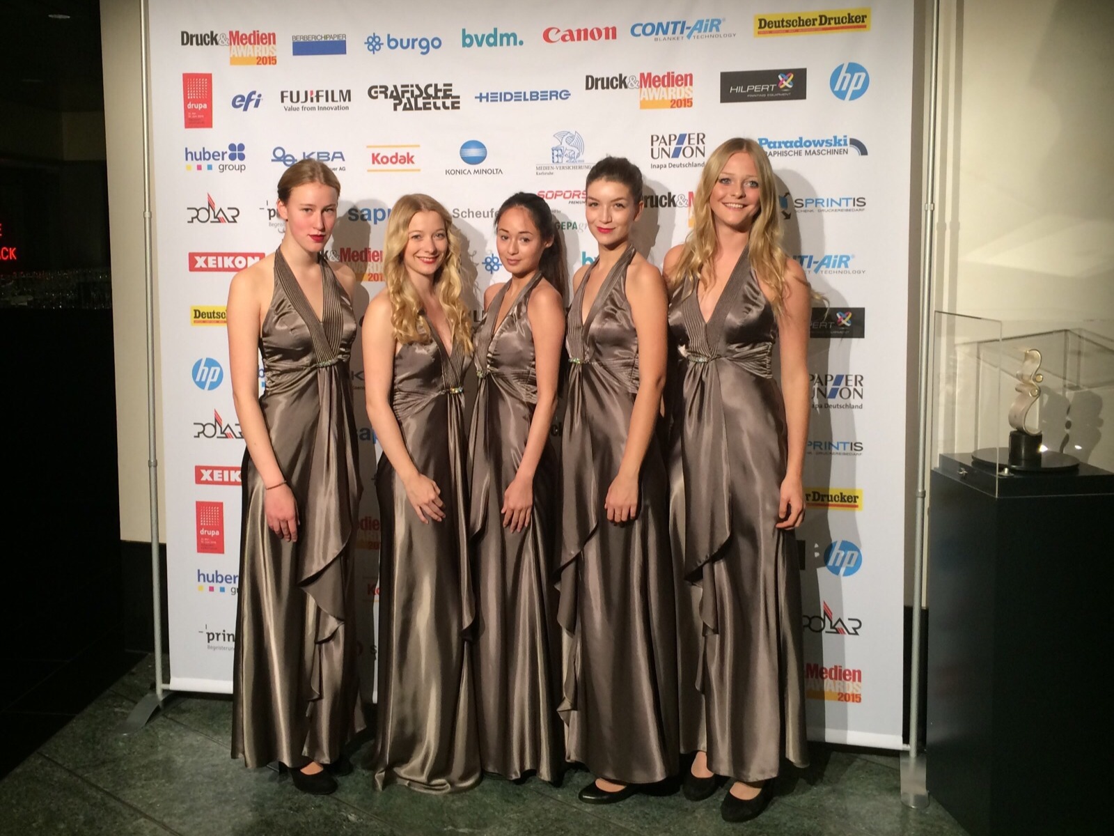 Vier Modelhostessen in eleganten Abendkleidern vor einer Fotowand, lächelnder Auftritt bei Gala, Event und exklusiver Markenpräsentation