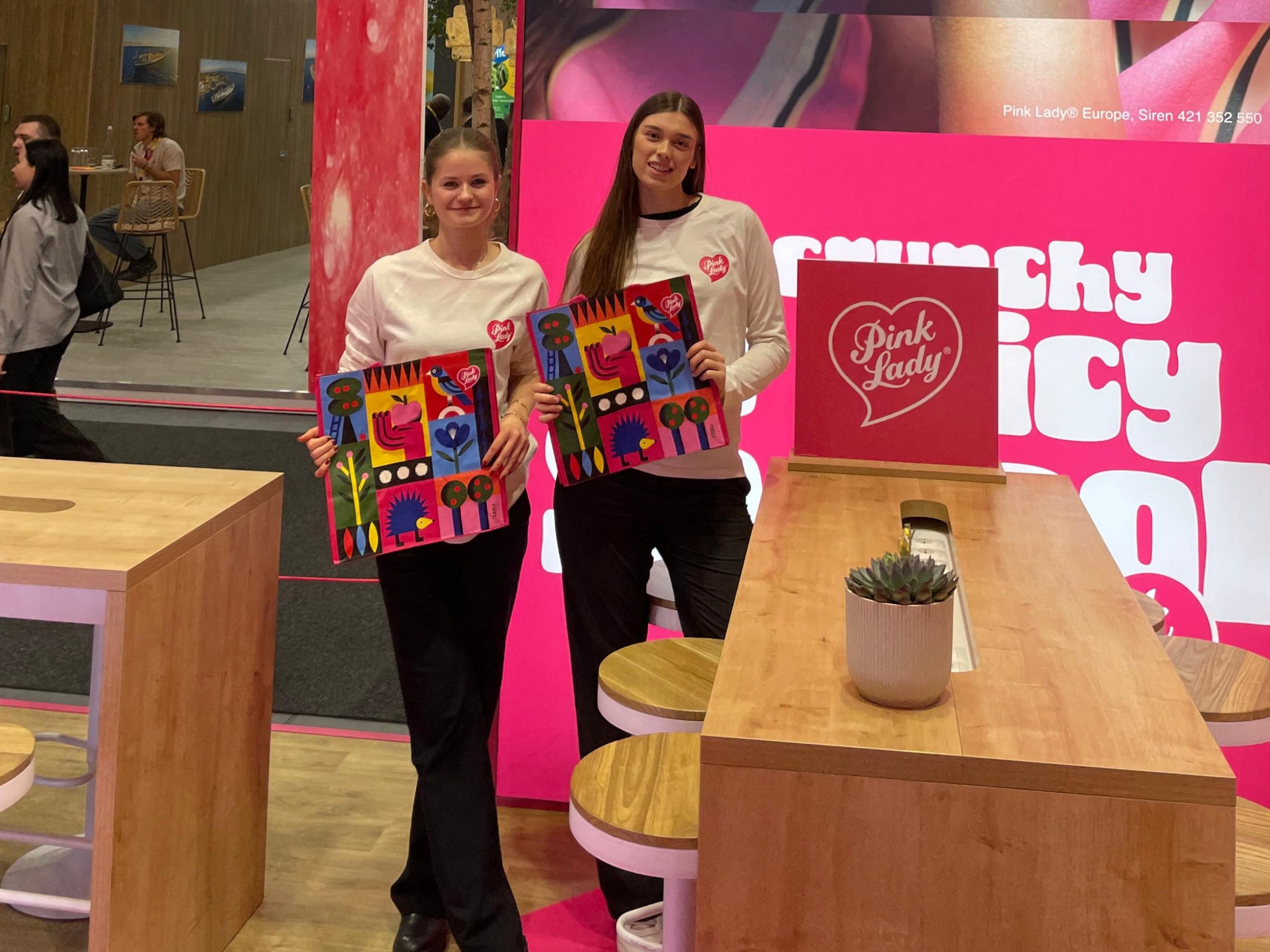 Zwei Messehostessen für die Pink Lady Promotion in weißen Oberteilen und schwarzen Hosen auf einer Messe, freundlicher Promotion Einsatz und Markenpräsentation von cinnamon