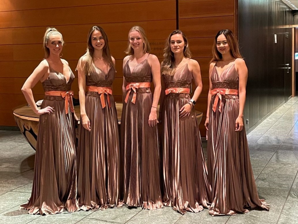 Fünf elegante Modelhostessen von cinnamon in stilvollen Abendkleidern bei einem Event, glamouröser Auftritt mit halb hochgesteckten Haaren und professioneller Ausstrahlung