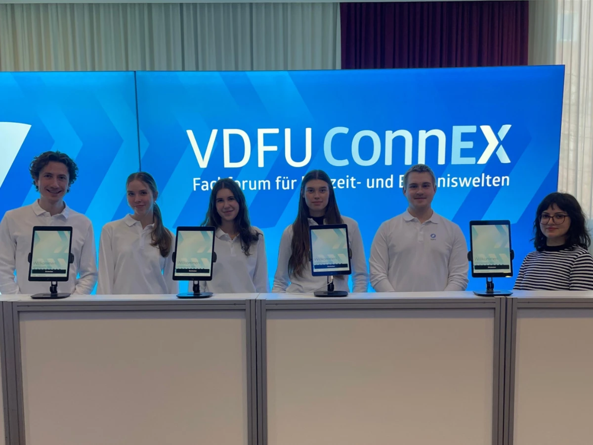 Sechs Hosts und Hostessen in weißen Longsleeves an der Akkreditierung vor blauer Fotowand in Freiburg, professioneller Check-in und Gästeservice bei Event und Messe