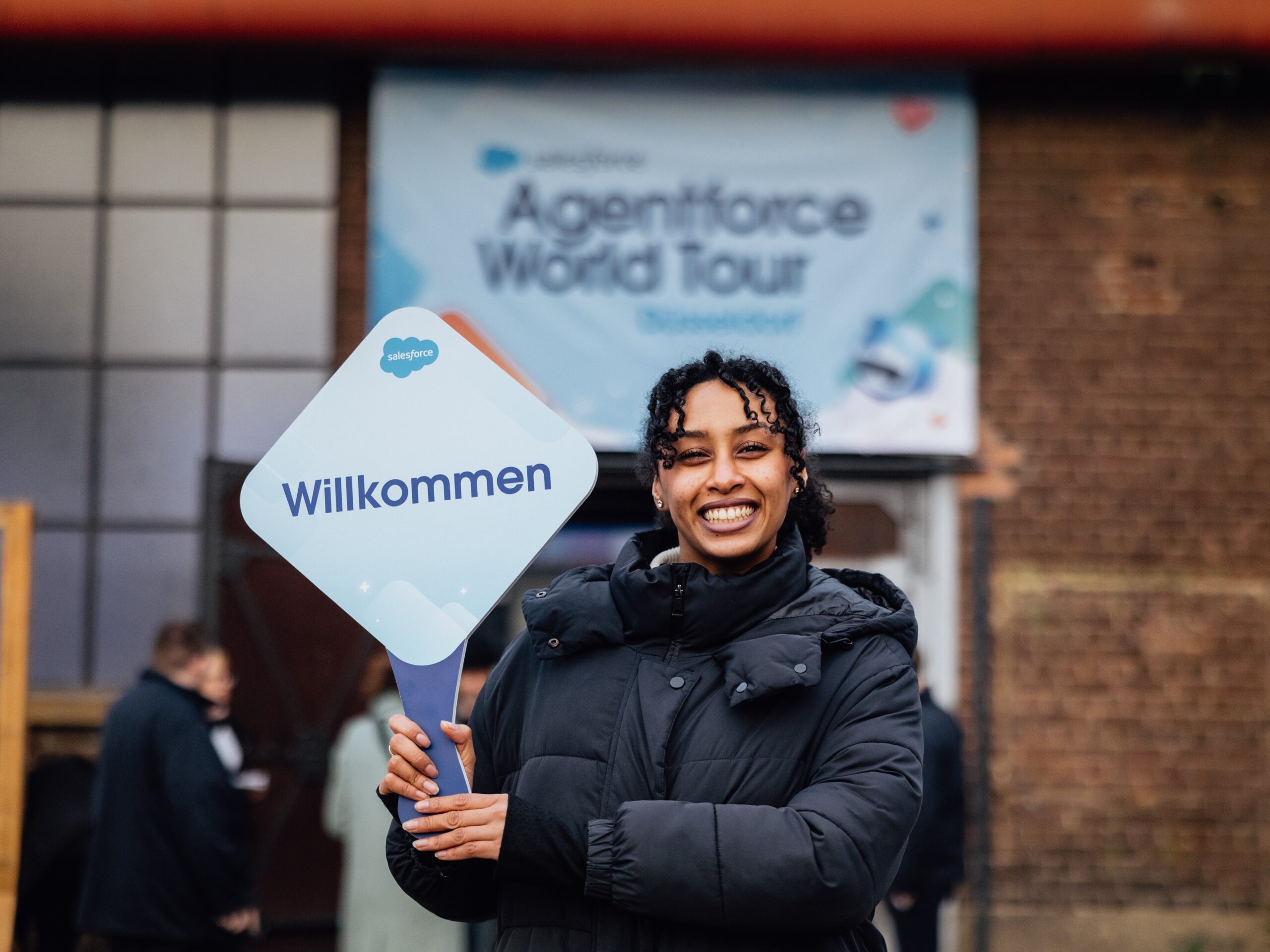 Lächelnde Messehostess mit Willkommensschild in den Händen, freundliche Wegeleitung und Gästebetreuung bei Event, Messe und Konferenz