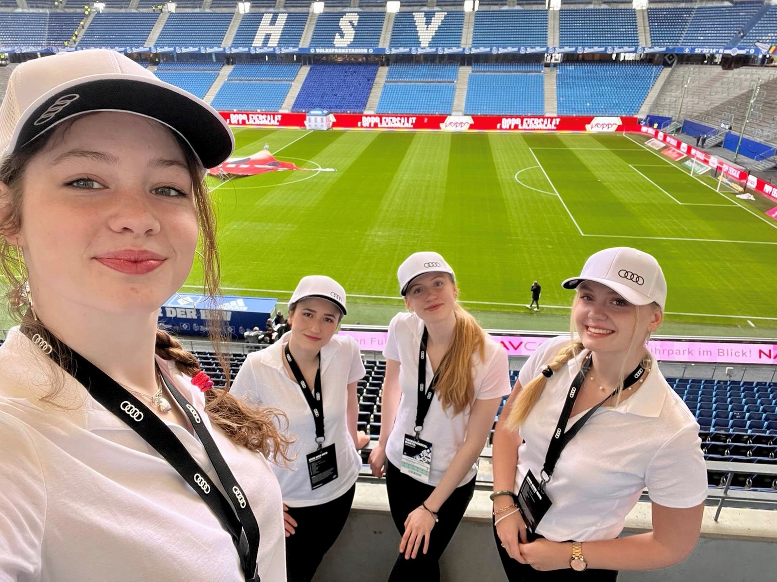 Vier Hostessen im Stadion mit weißen Poloshirts, Caps und Badges lächeln in die Kamera, Zimties Promotion Einsatz bei Sportevent und Markenaktion