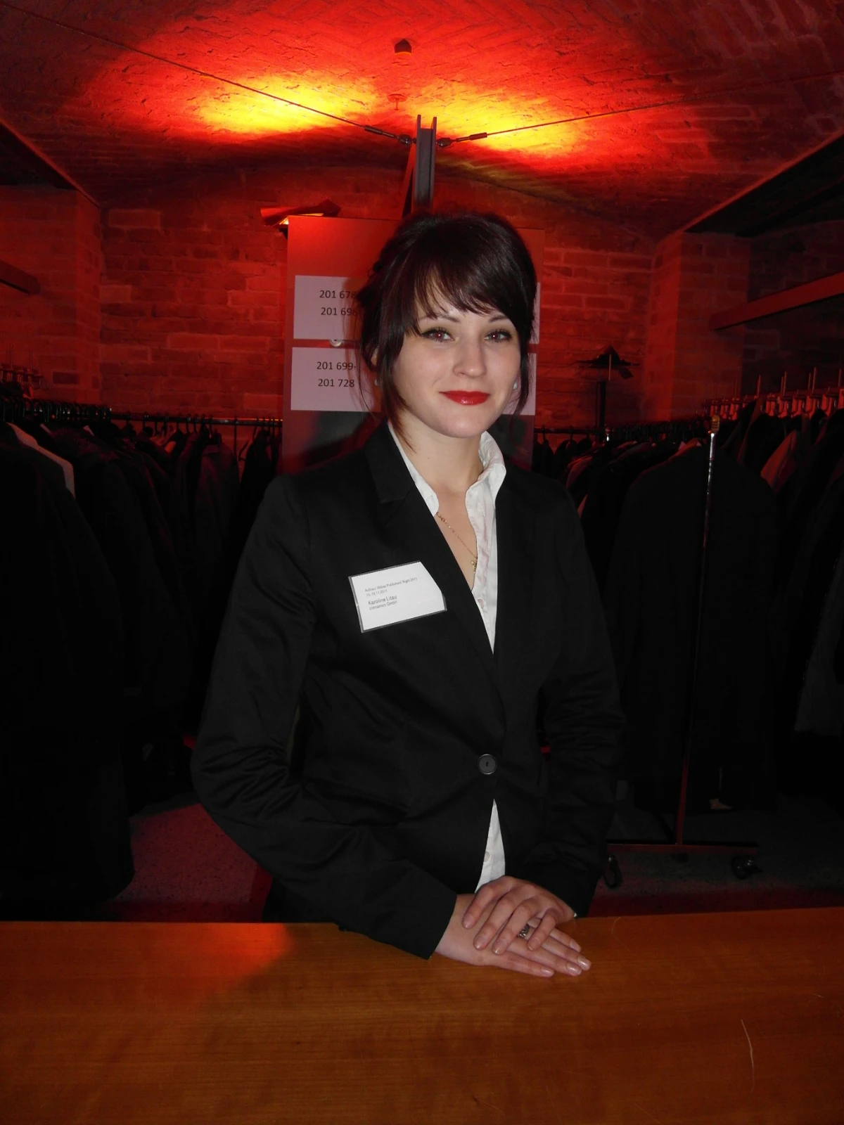 Hostess im schwarzen Business-Outfit am Garderobentresen