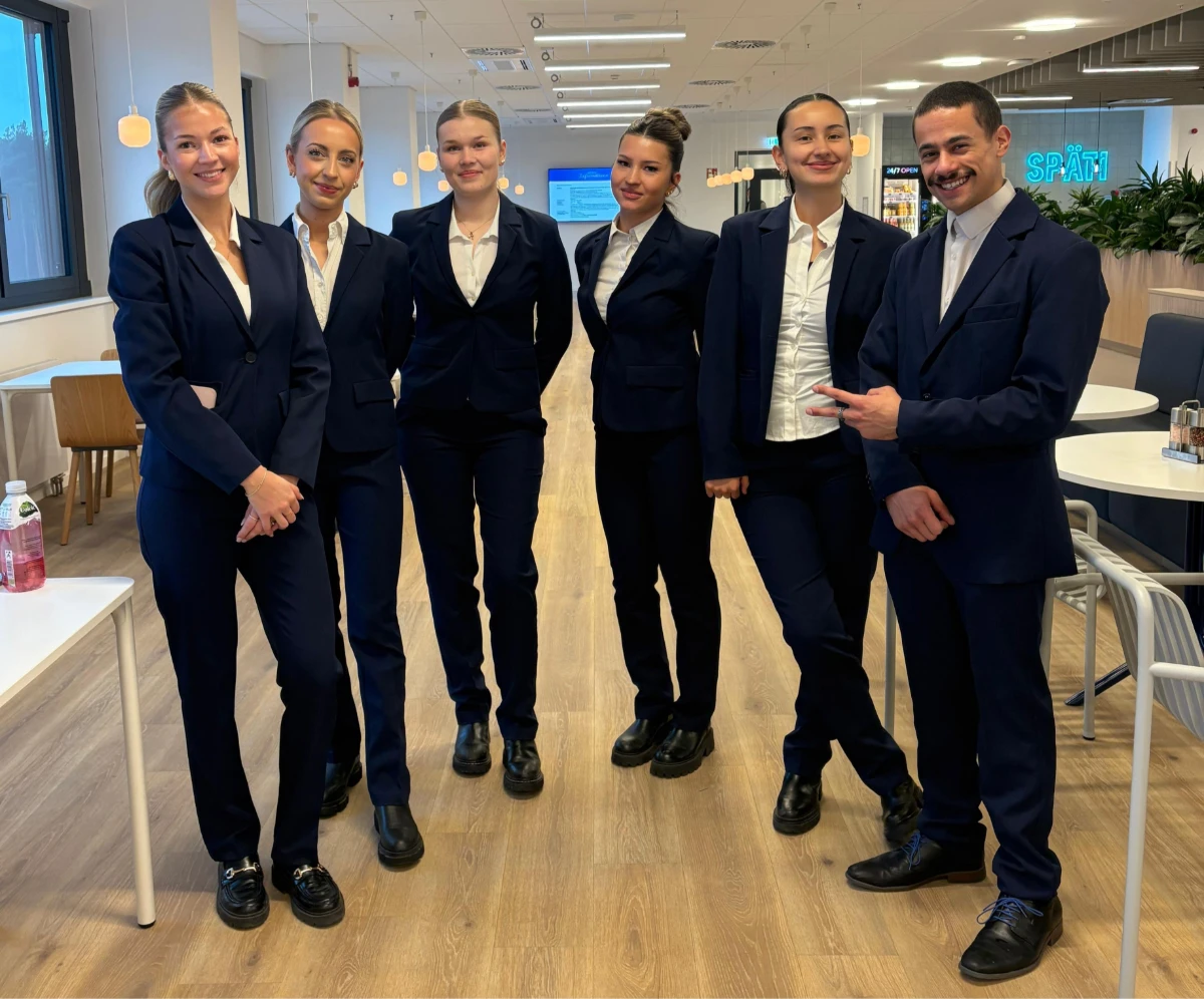 Hosts und Hostessen in eleganten Business-Outfits mit schwarzem Anzug und weißem Hemd lächeln in die Kamera, professioneller Empfangsservice bei Event und Messe