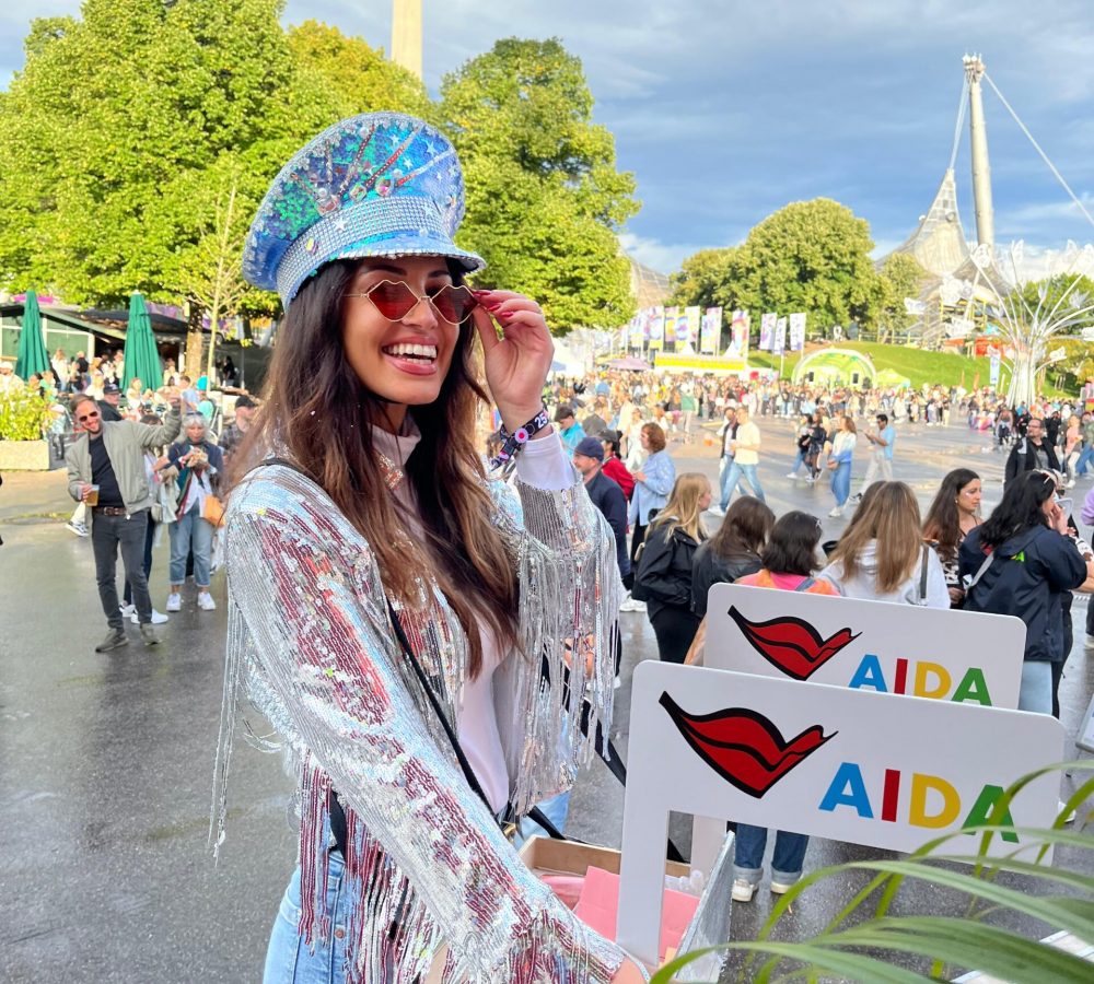 Promotion Hostess mit Bauchladen im Glitzer-Outfit läuft über ein Festival, lächelnder Einsatz bei AIDA Promotion und Markenaktivierung