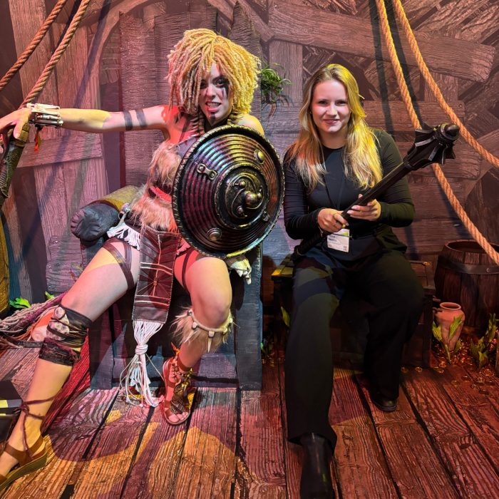 Hostess in schwarzem Outfit sitzt neben einem Walking Act im Wikingerkostüm auf der gamescom in Köln, kreative Promotion und Entertainment mit cinnamon