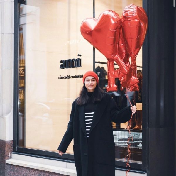 Hostess mit rotem Herz-Luftballon vor einem AMI Store in Stuttgart, stilvolle Sampling Promotion von cinnamon im schwarzen Mantel und roter Mütze
