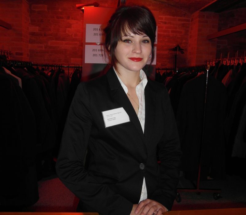 Modelhostess im schwarzen Blazer mit weißem Hemd hinter einem Garderoben-Tresen, eleganter Empfangsservice bei Event, Gala und Veranstaltung