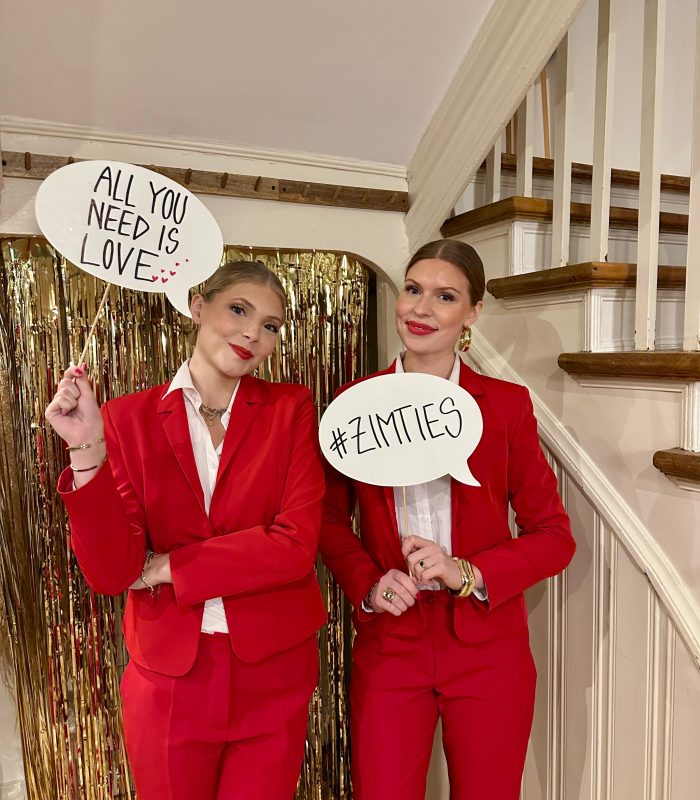 Zwei Hostessen in roten Hosenanzügen vor goldenem Vorhang halten Sprechblasen-Schilder, kreative Promotion Aktion bei Event und Markeninszenierung