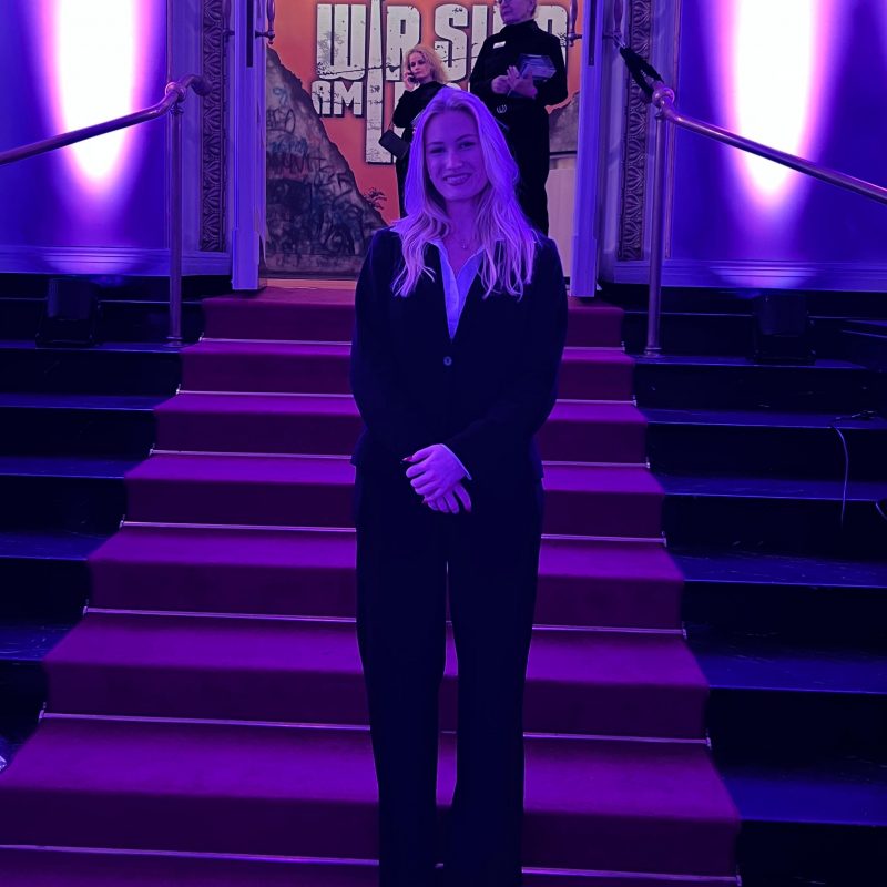 Hostess im schwarzen Hosenanzug vor einem Eingang, eleganter Empfangsservice bei Event, Gala und professioneller Veranstaltung