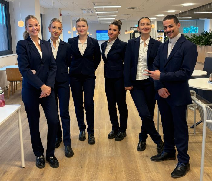 Hosts und Hostessen in eleganten Business-Outfits mit schwarzem Anzug und weißem Hemd lächeln in die Kamera, professioneller Empfangsservice bei Event und Messe