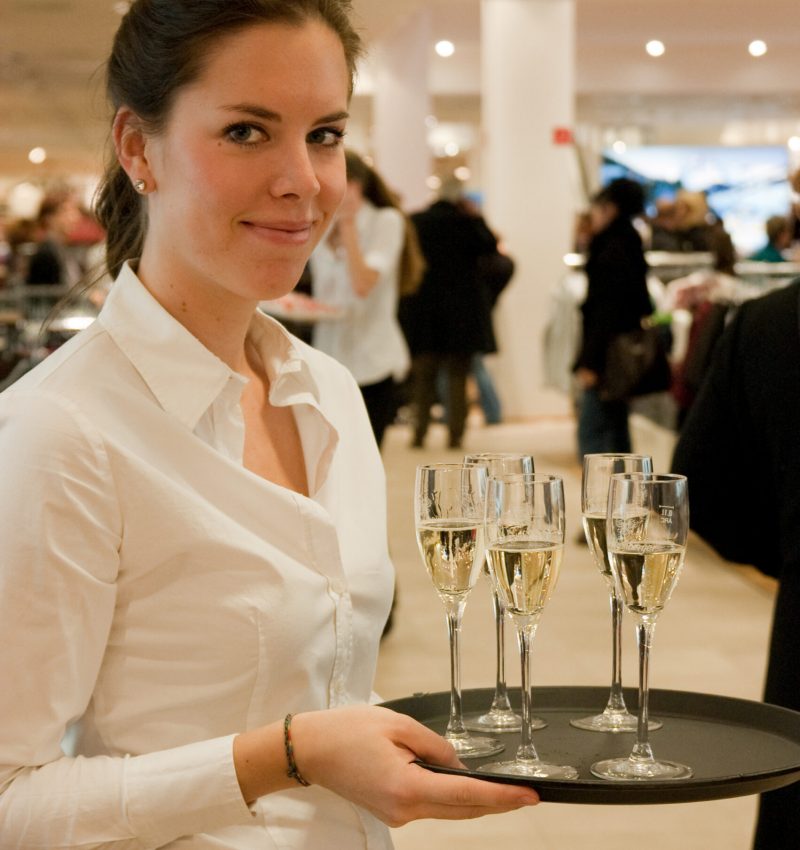 Catering Hostess im weißen Hemd mit Tablet und Gläsern, Haare zusammengebunden, lächelnder Service bei Event, Gala und Veranstaltung